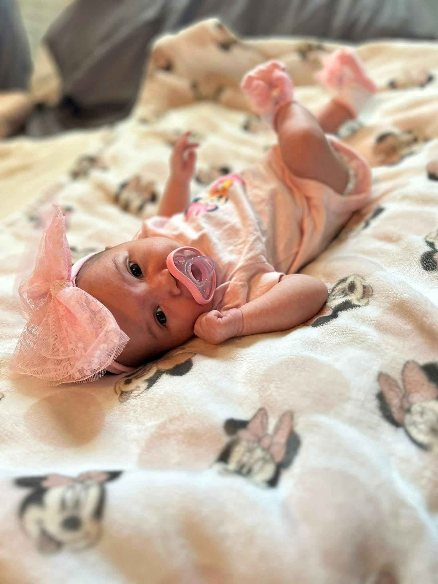 Baby lying on a patterned blanket with a pacifier and a large hair bow