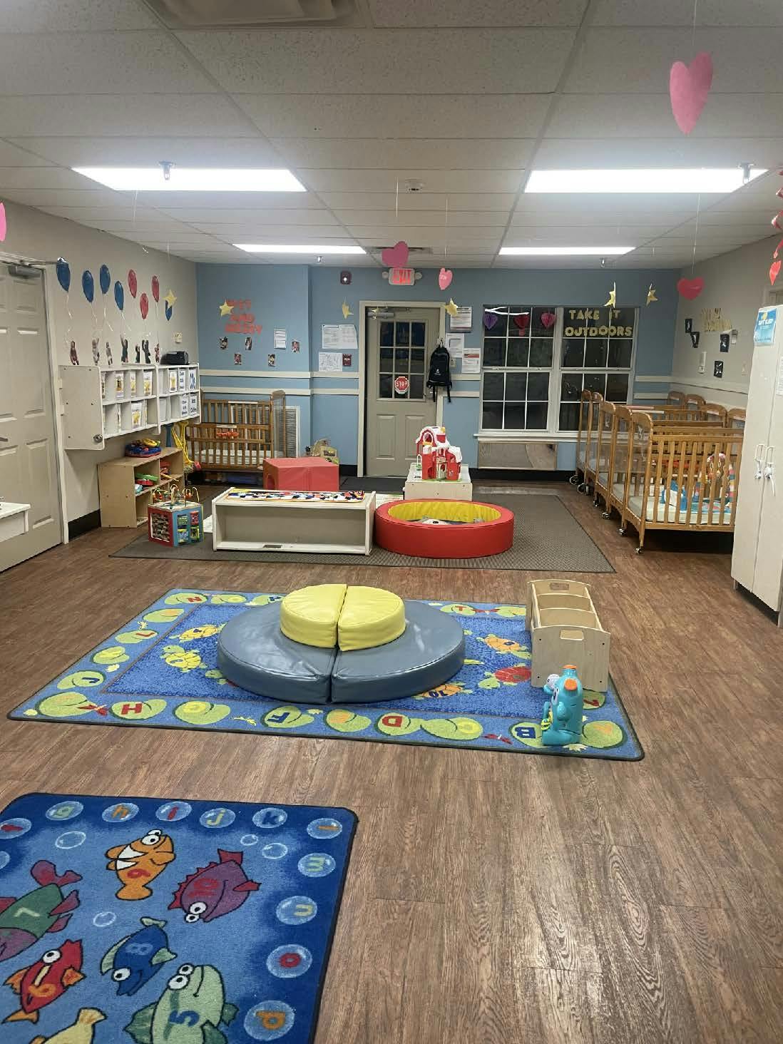 A colorful empty classroom with cribs, play mats, and learning toys