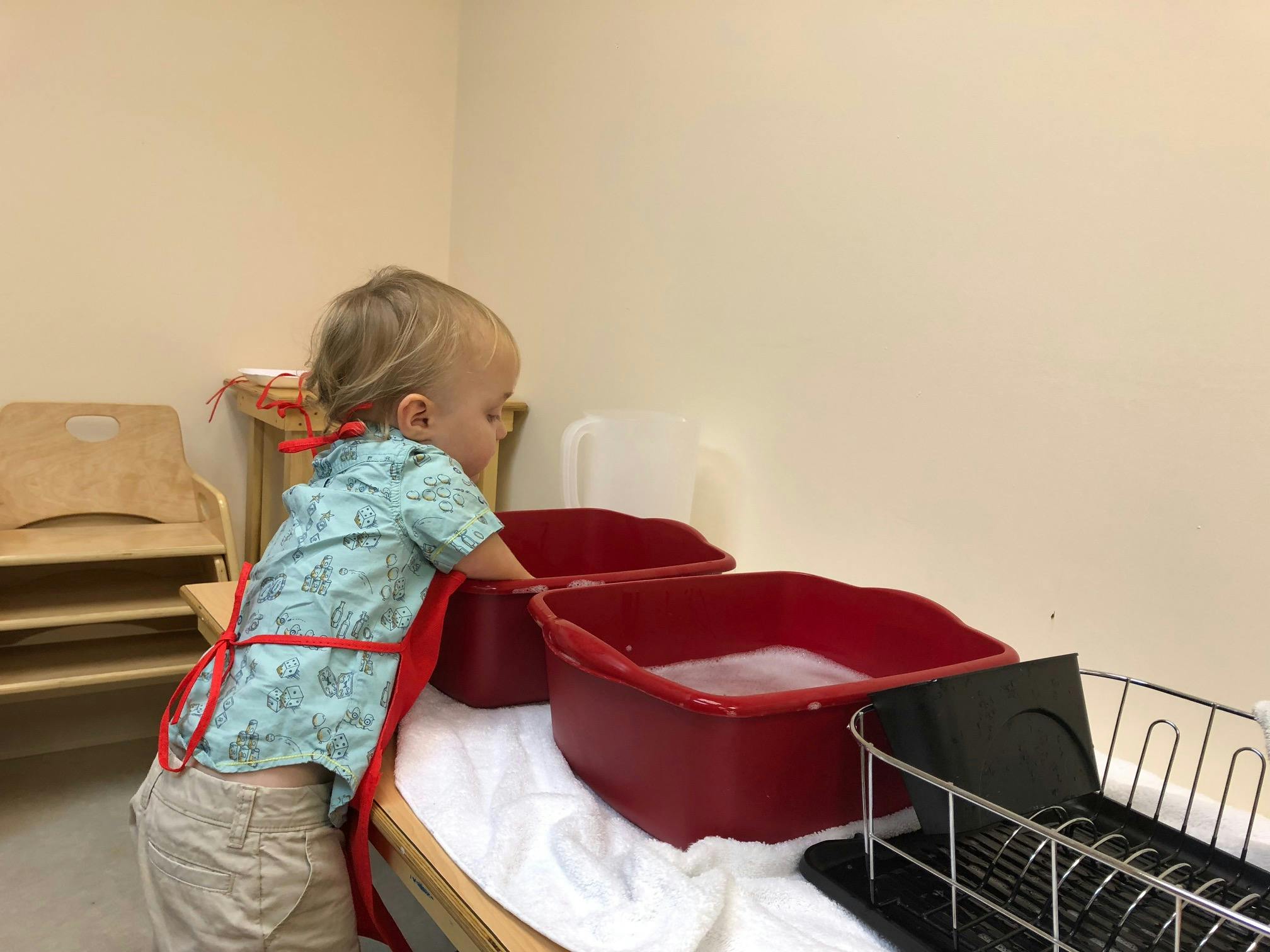 Child in an apron washing dishes in red tubs