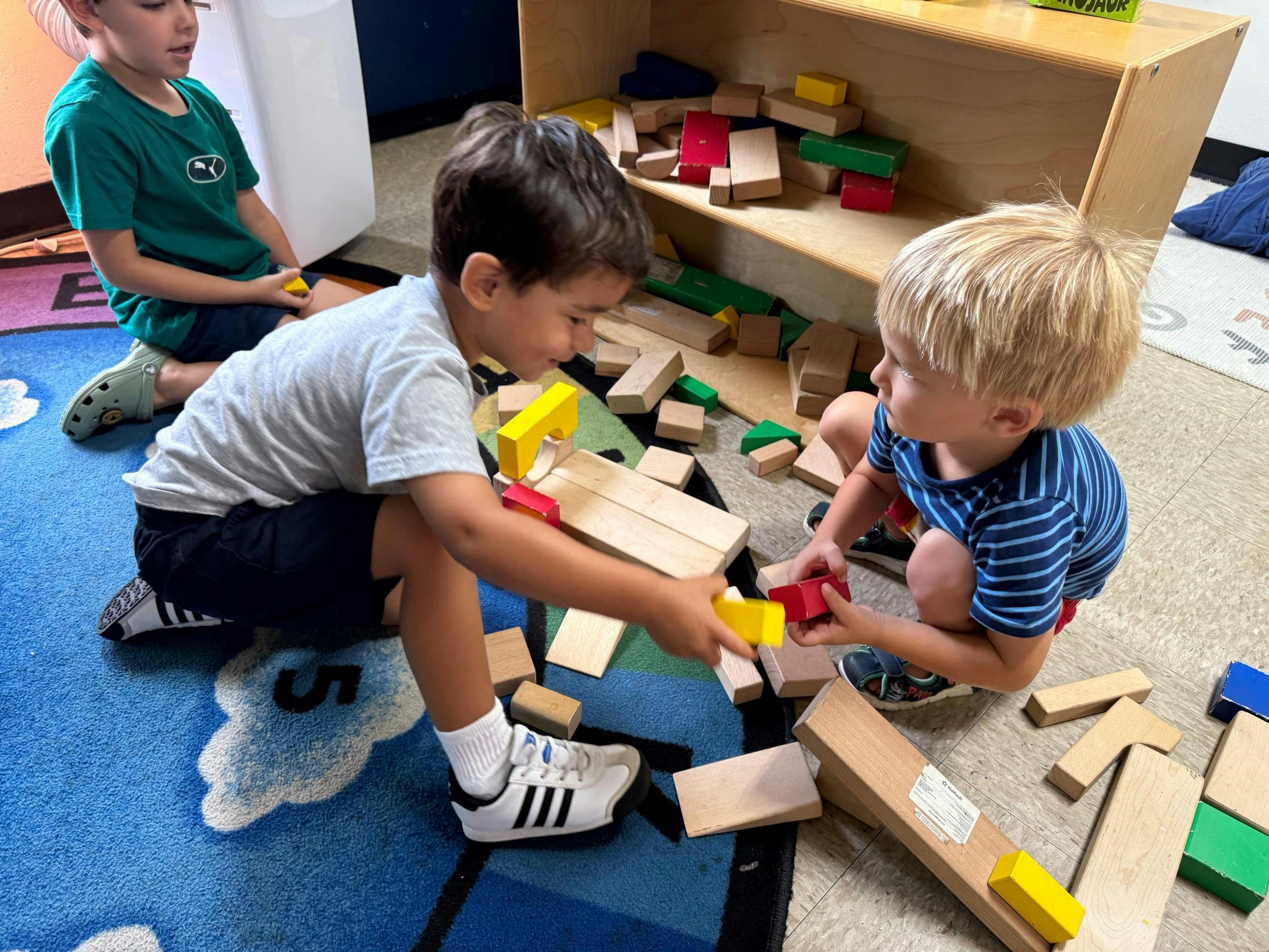 Three children playing with colorful building blocks on a rug