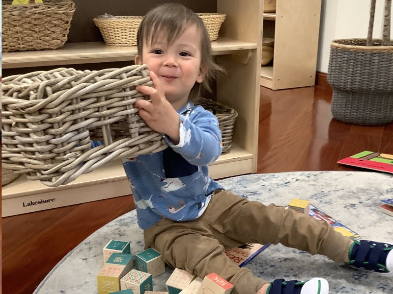 Child sitting on a rug, holding a woven basket and smiling