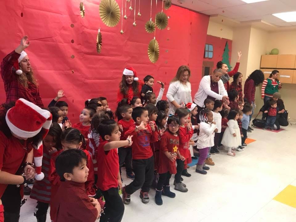 Adults and children in a classroom, some wearing Santa hats
