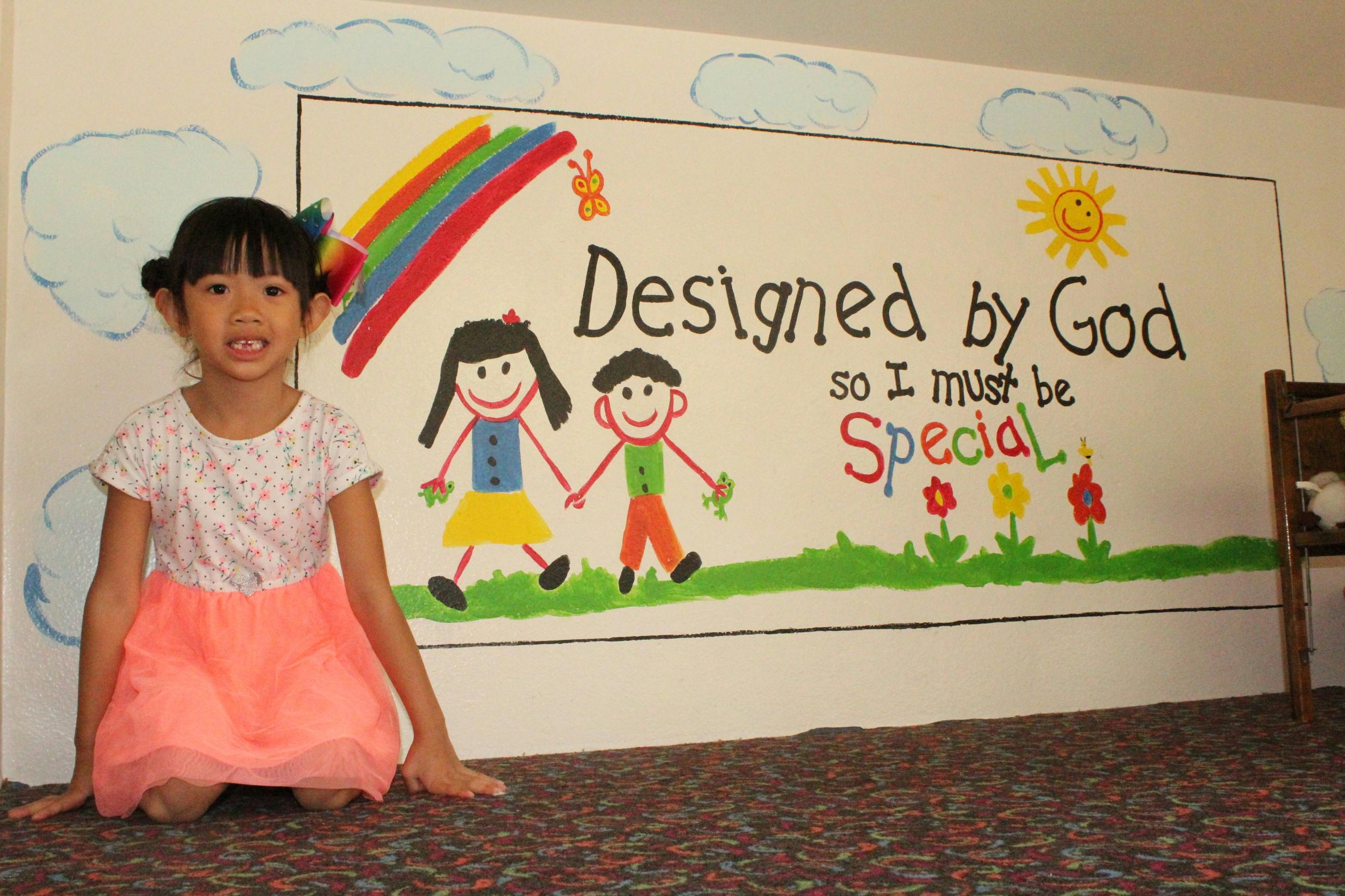 Child kneeling in front of a wall mural with text "Designed by God so I must be Special"