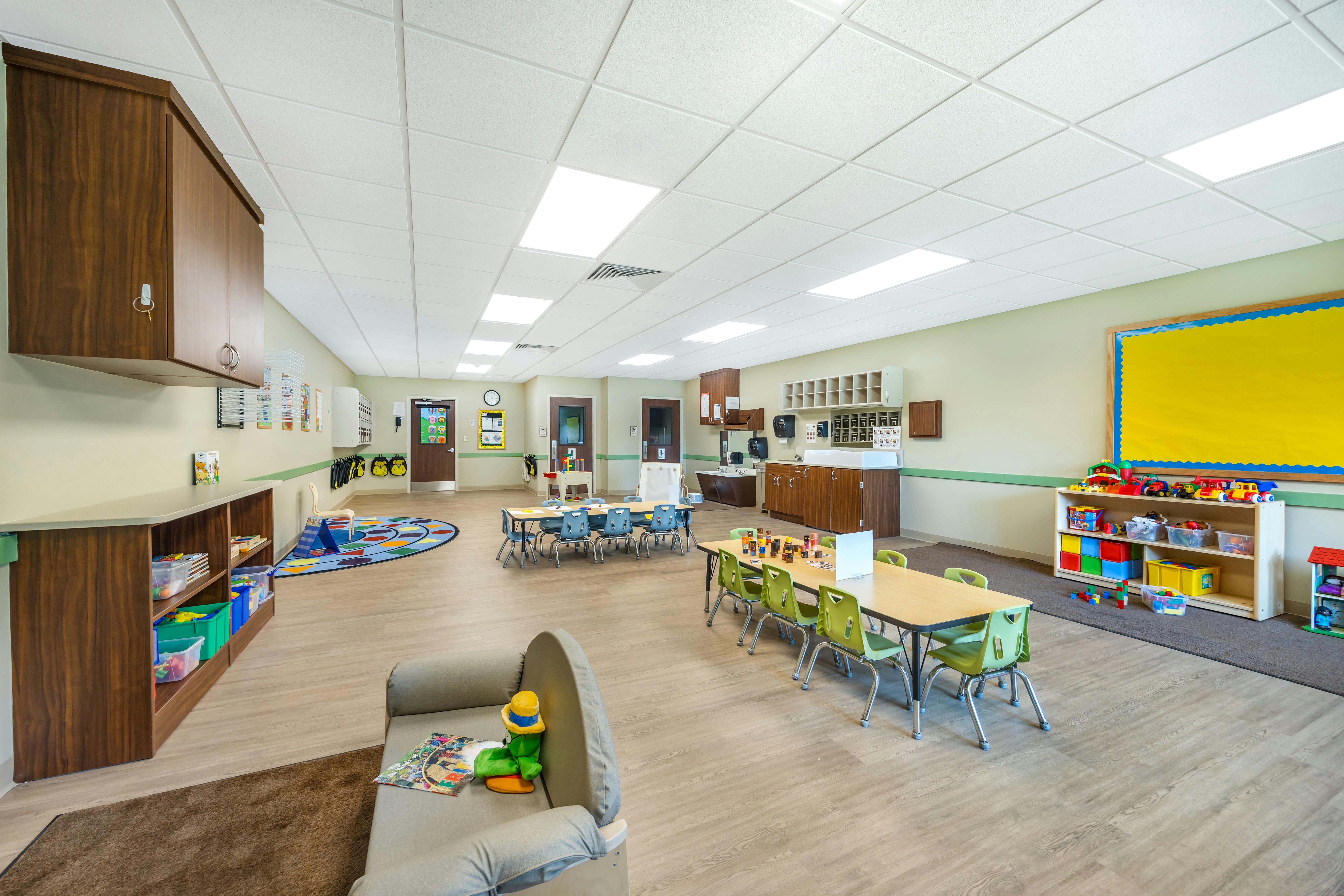 A brightly lit classroom with small tables, chairs, and play areas