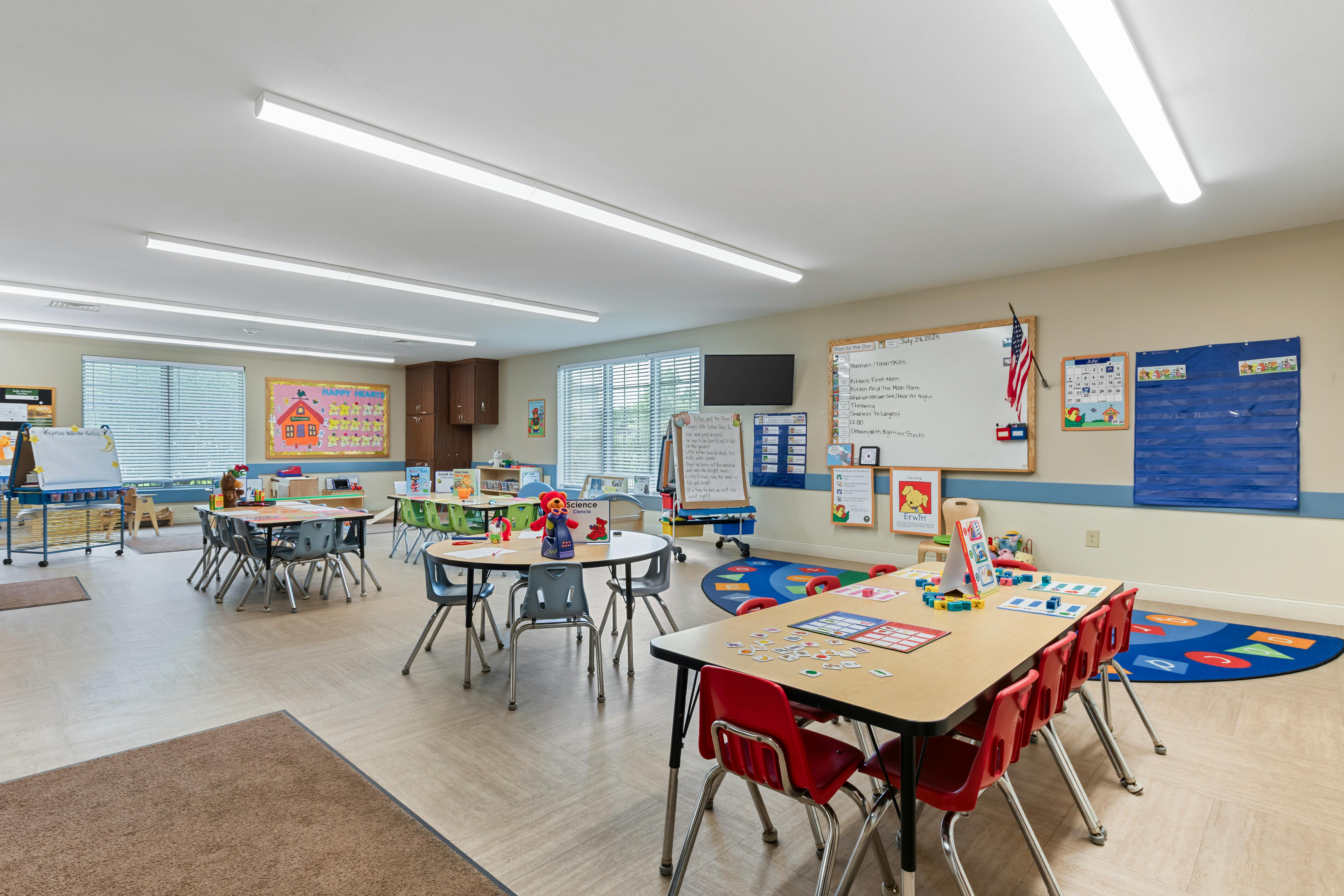 An empty classroom with several small tables and chairs, and learning materials