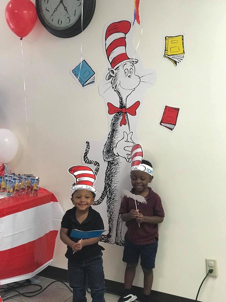Two children wearing striped hats standing in front of a Cat in the Hat drawing
