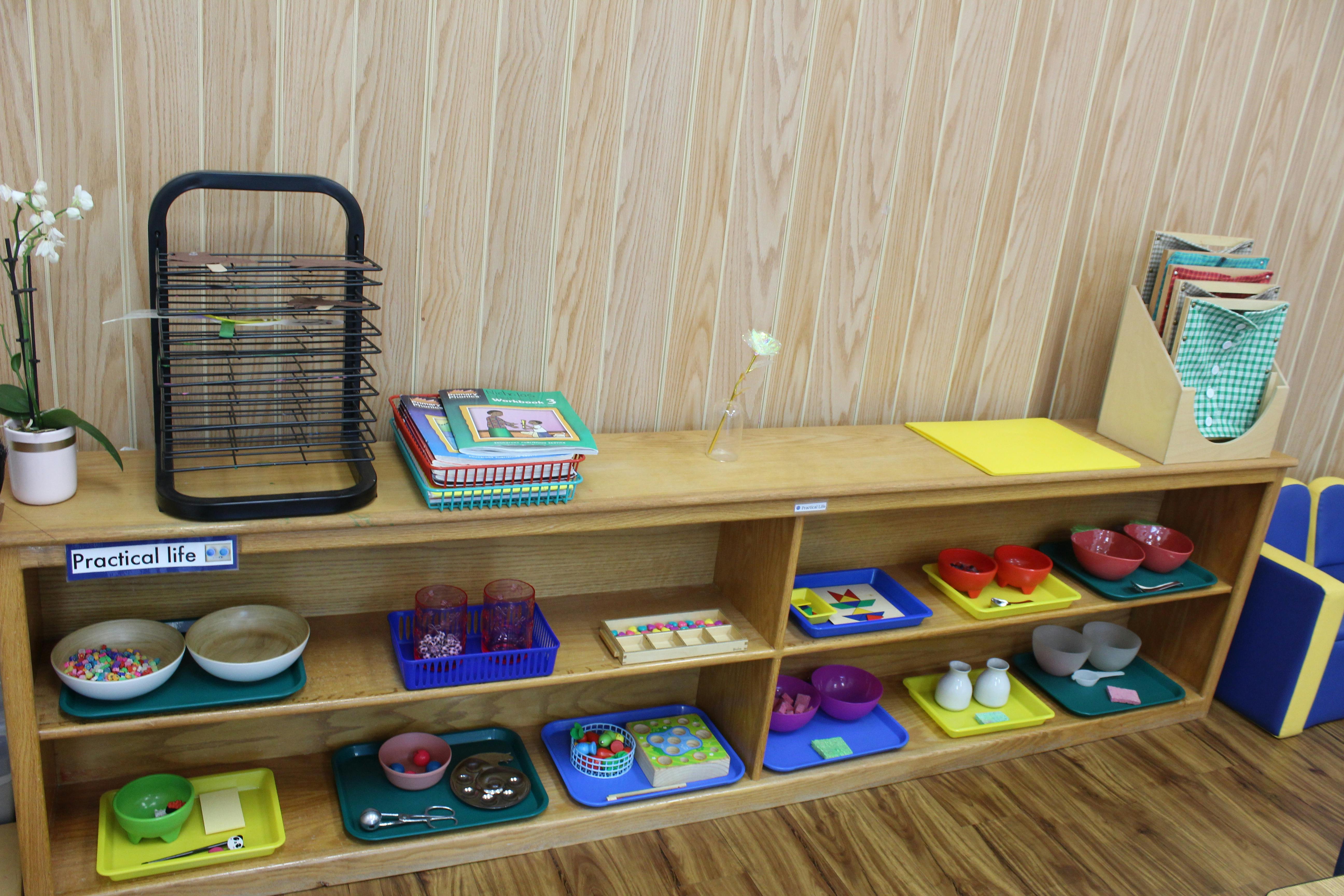 Classroom shelf with "Practical life" sign and various activity trays
