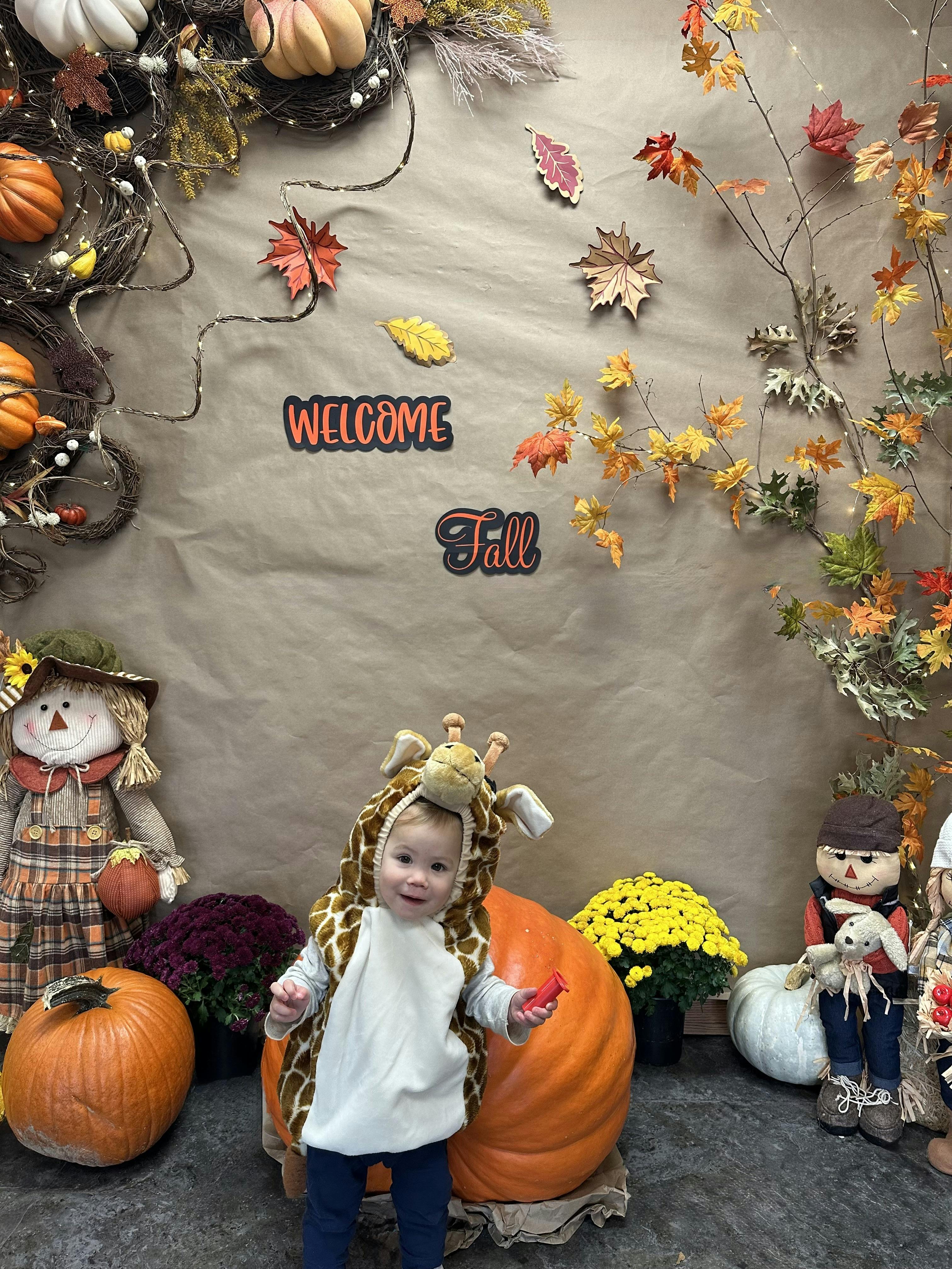 Child in giraffe costume standing next to pumpkins and fall decorations