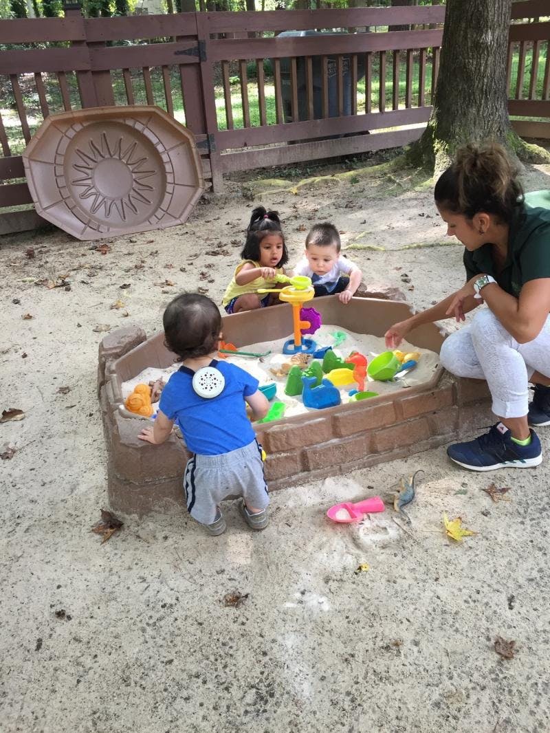 Adult and three children playing in a sandbox with toys