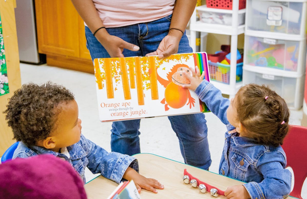 Person holding a book for two children at a table