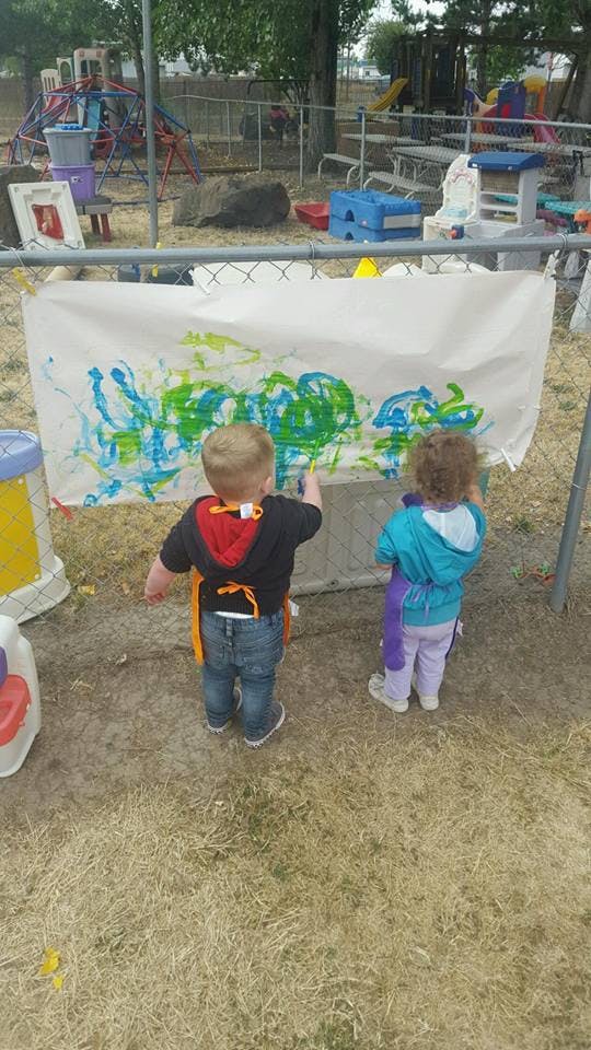 Two children painting on a white sheet outdoors