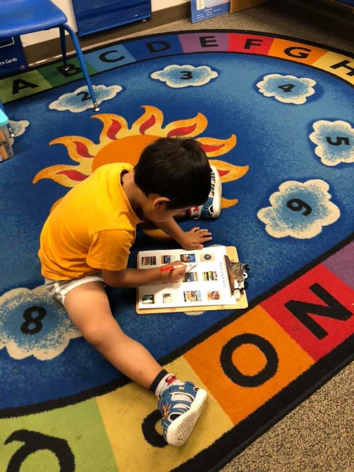 Child sitting on a colorful rug, writing on a clipboard