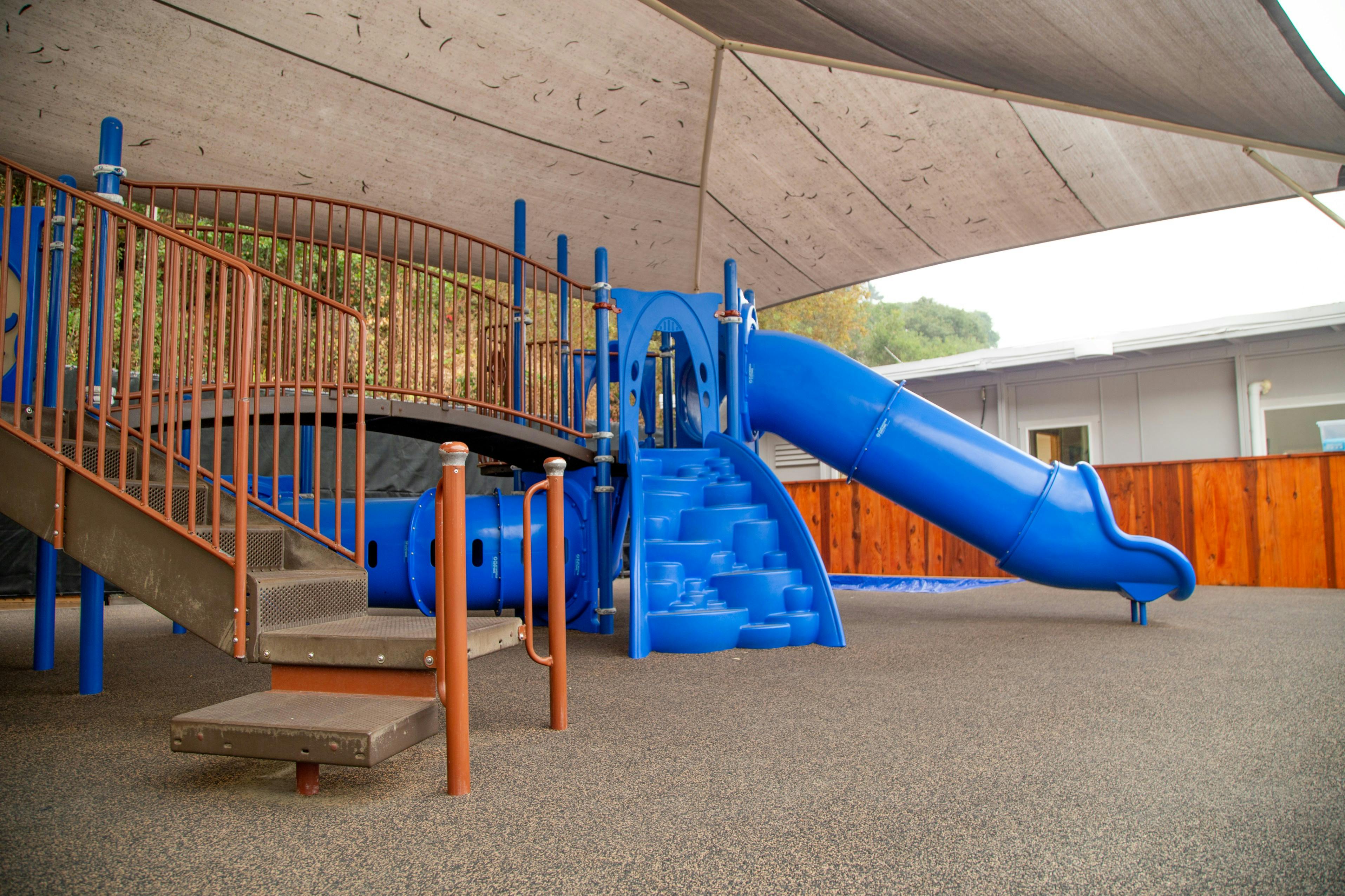 Playground with blue slide and climbing structure under a shade canopy