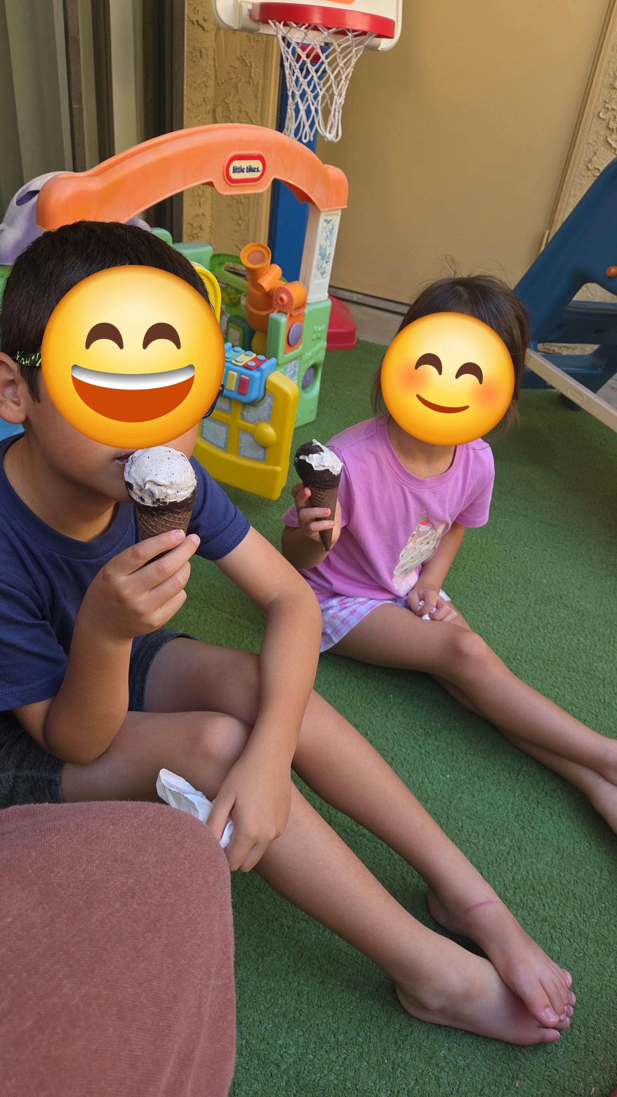 Two children sitting on artificial grass eating ice cream cones