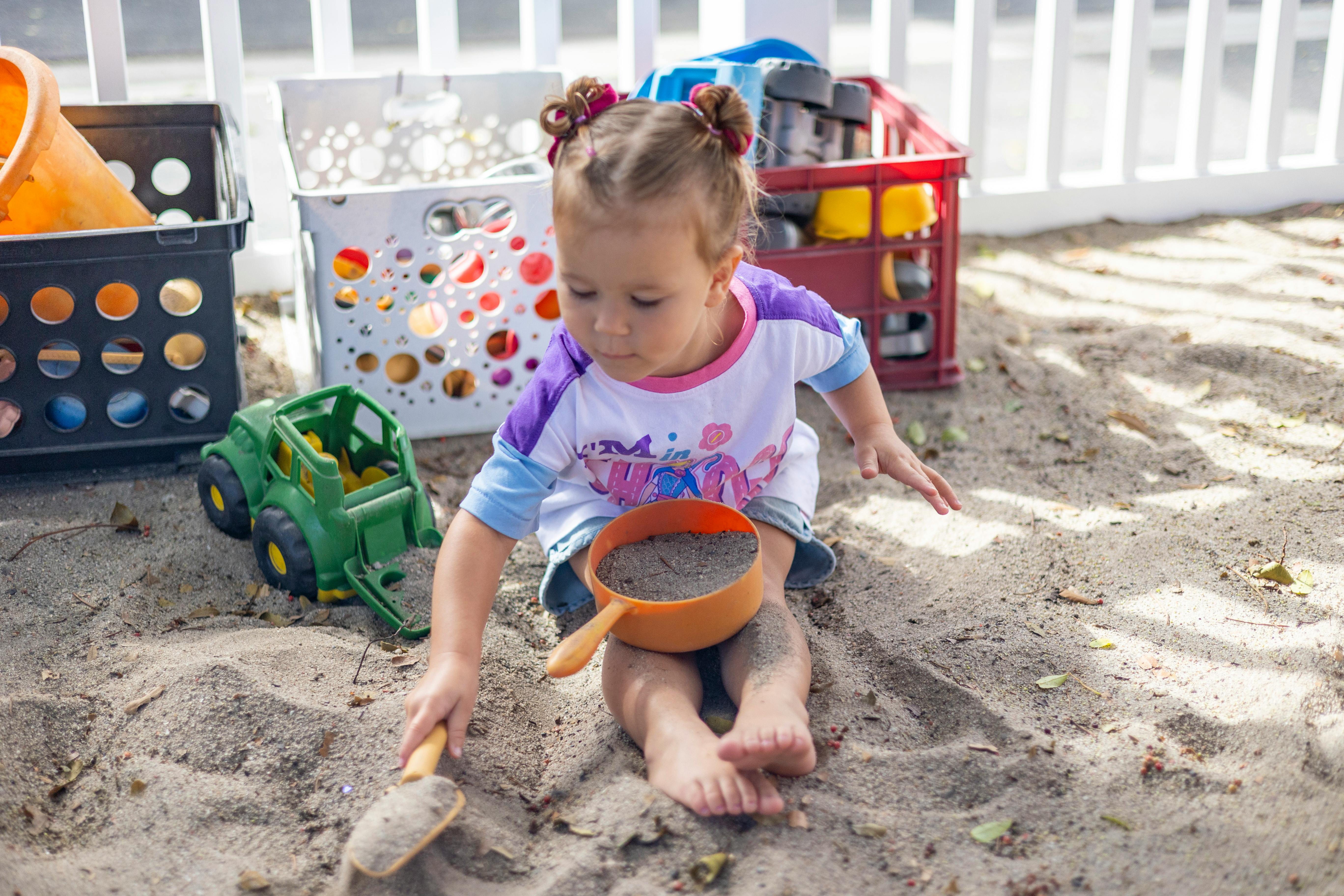 Child playing in sand with a shovel and a small pot of sand