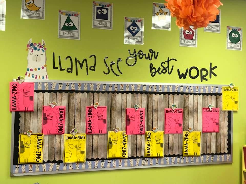 Classroom bulletin board with student work and a llama cutout