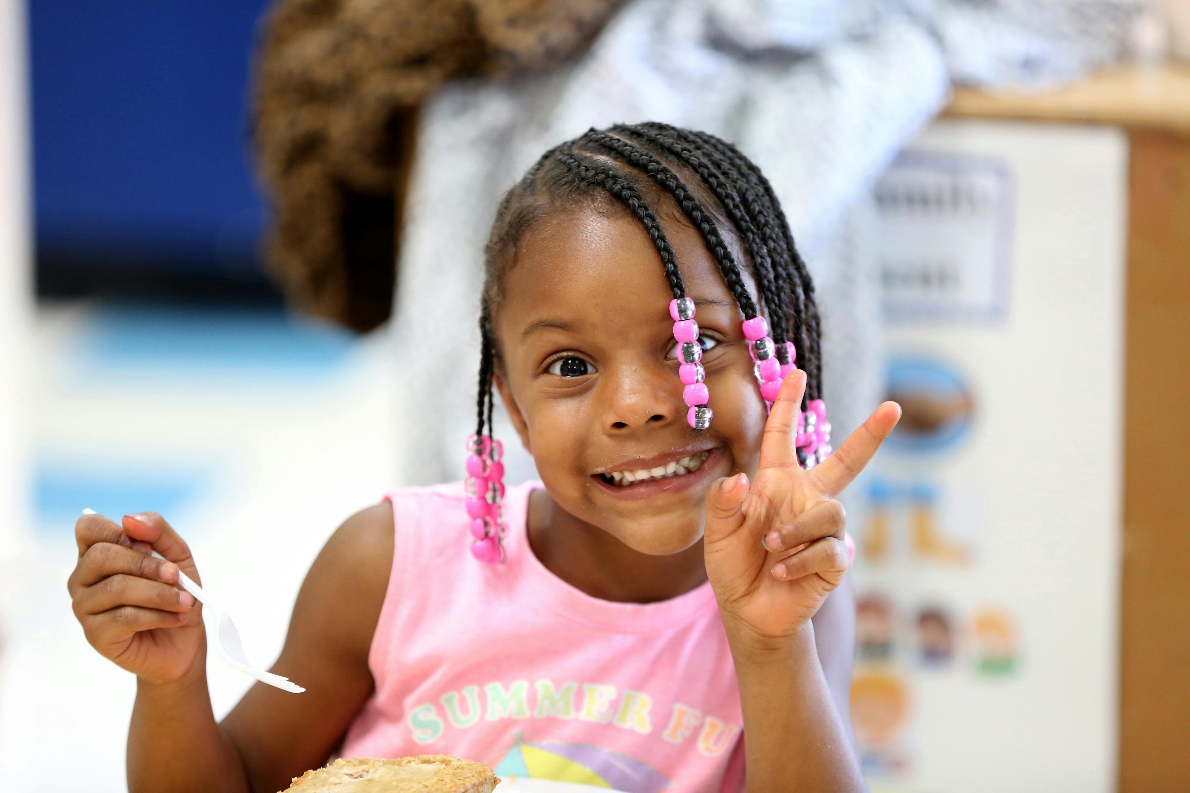 Child with braided hair holding up a peace sign
