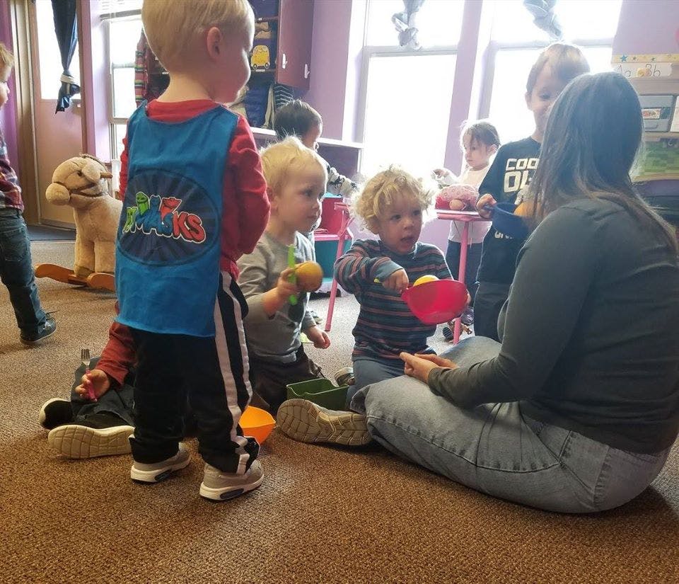 Adult sitting on floor with multiple children playing with toys