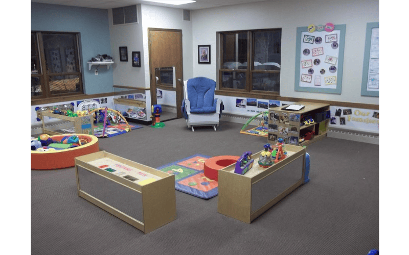 A childcare room with a blue rocking chair, play mats, toys, and activity tables