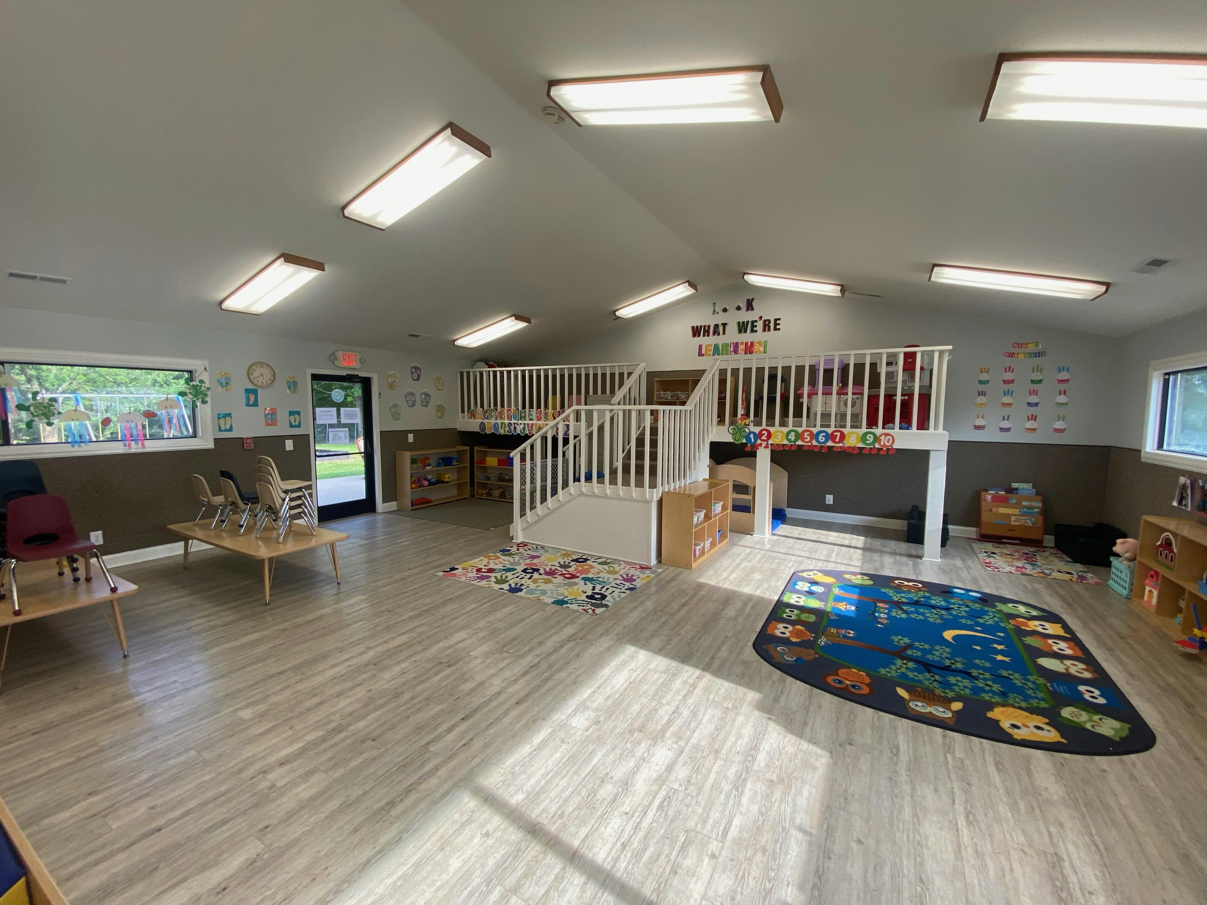 Classroom with child-sized tables and chairs, a play loft, and rugs on the floor