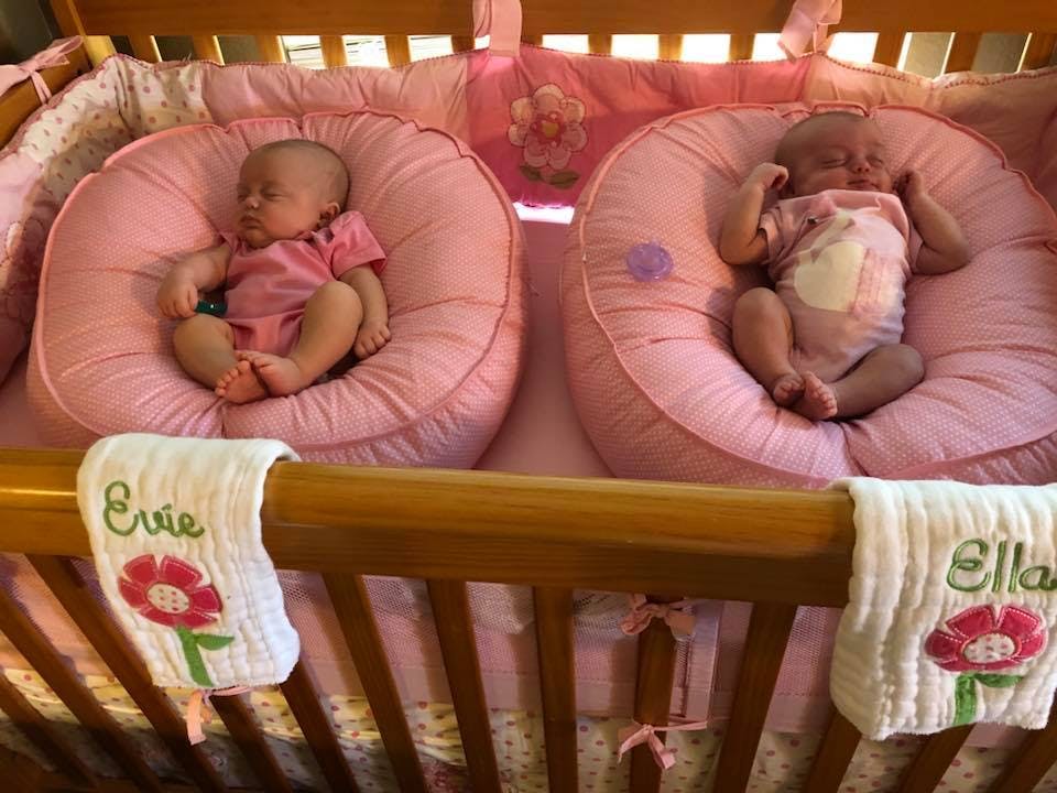 Two babies sleeping in pink round cushions in a crib