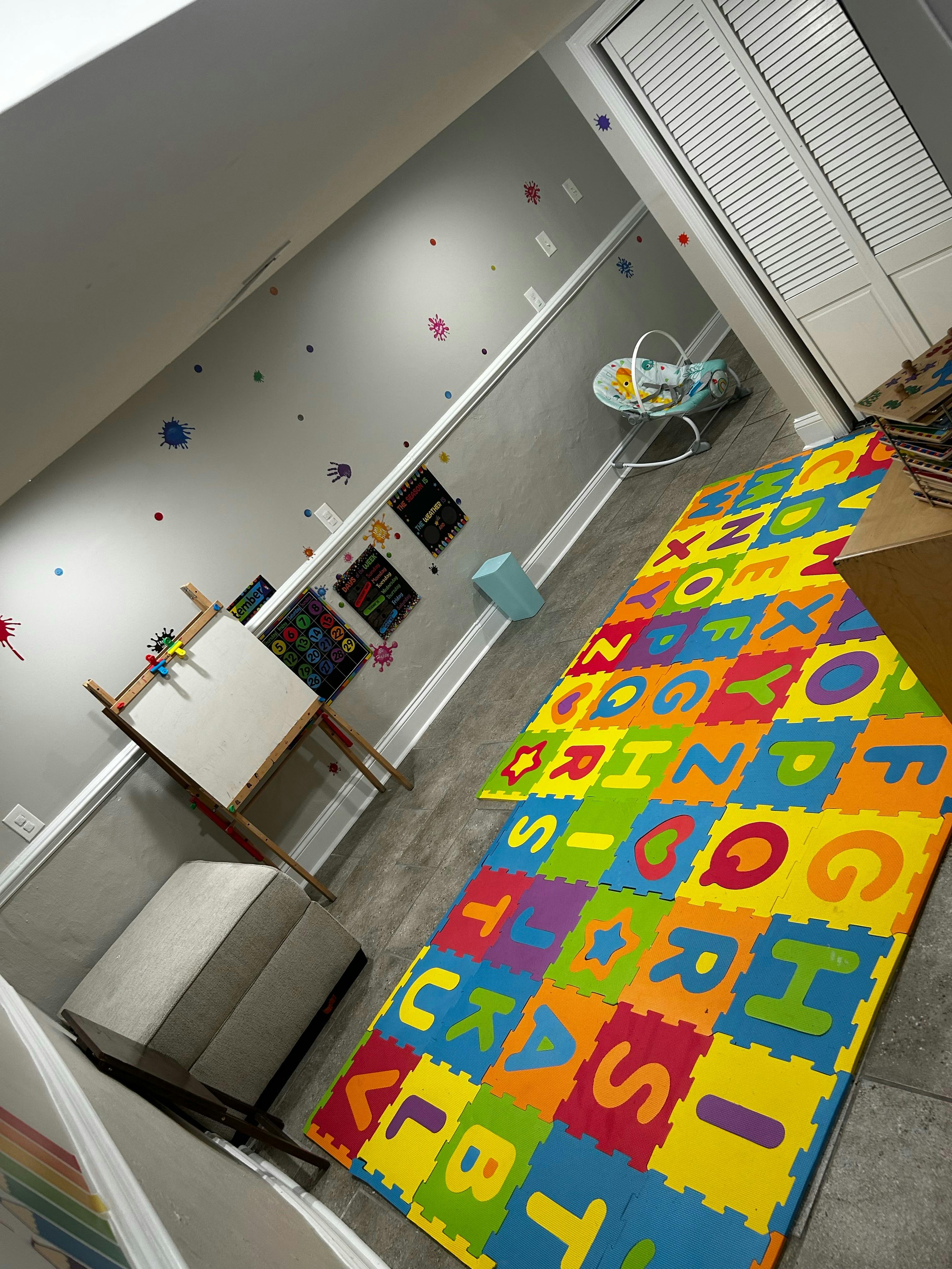 Playroom with alphabet mat, easel, and baby bouncer