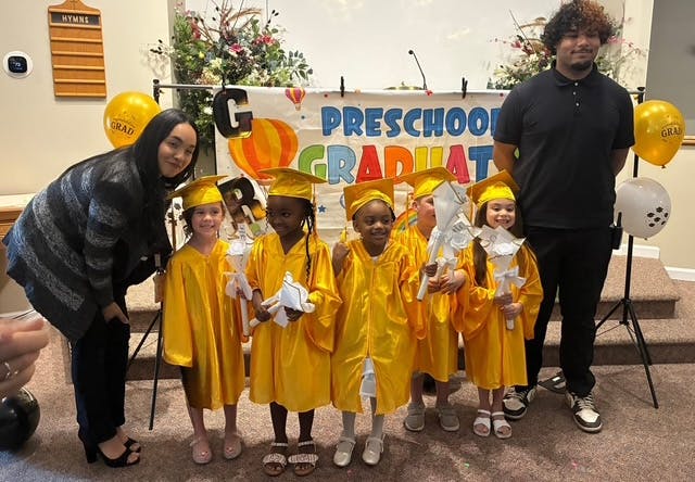 Group of children in yellow graduation gowns standing in front of a banner