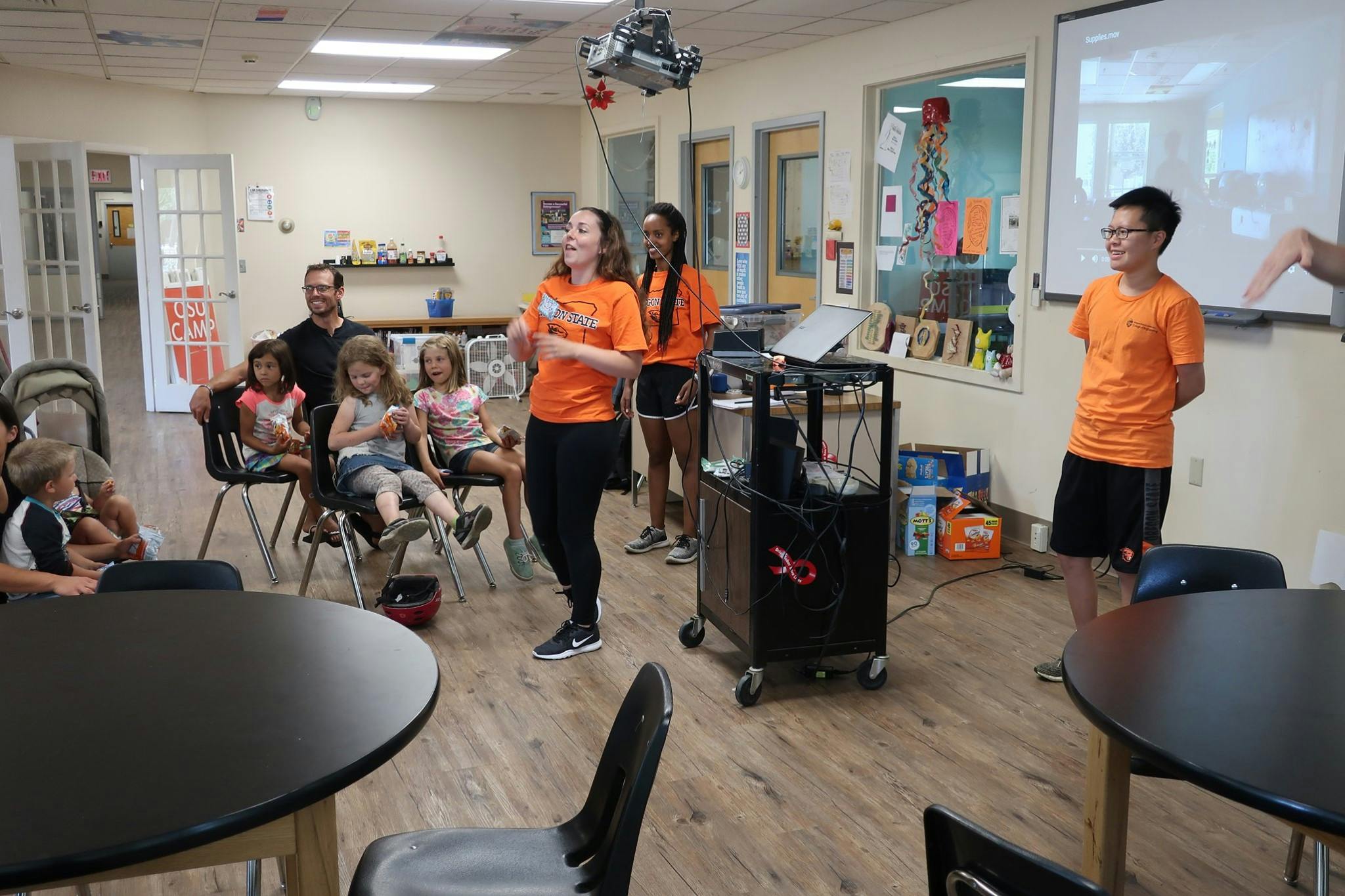 People and children in a room, some standing and some seated