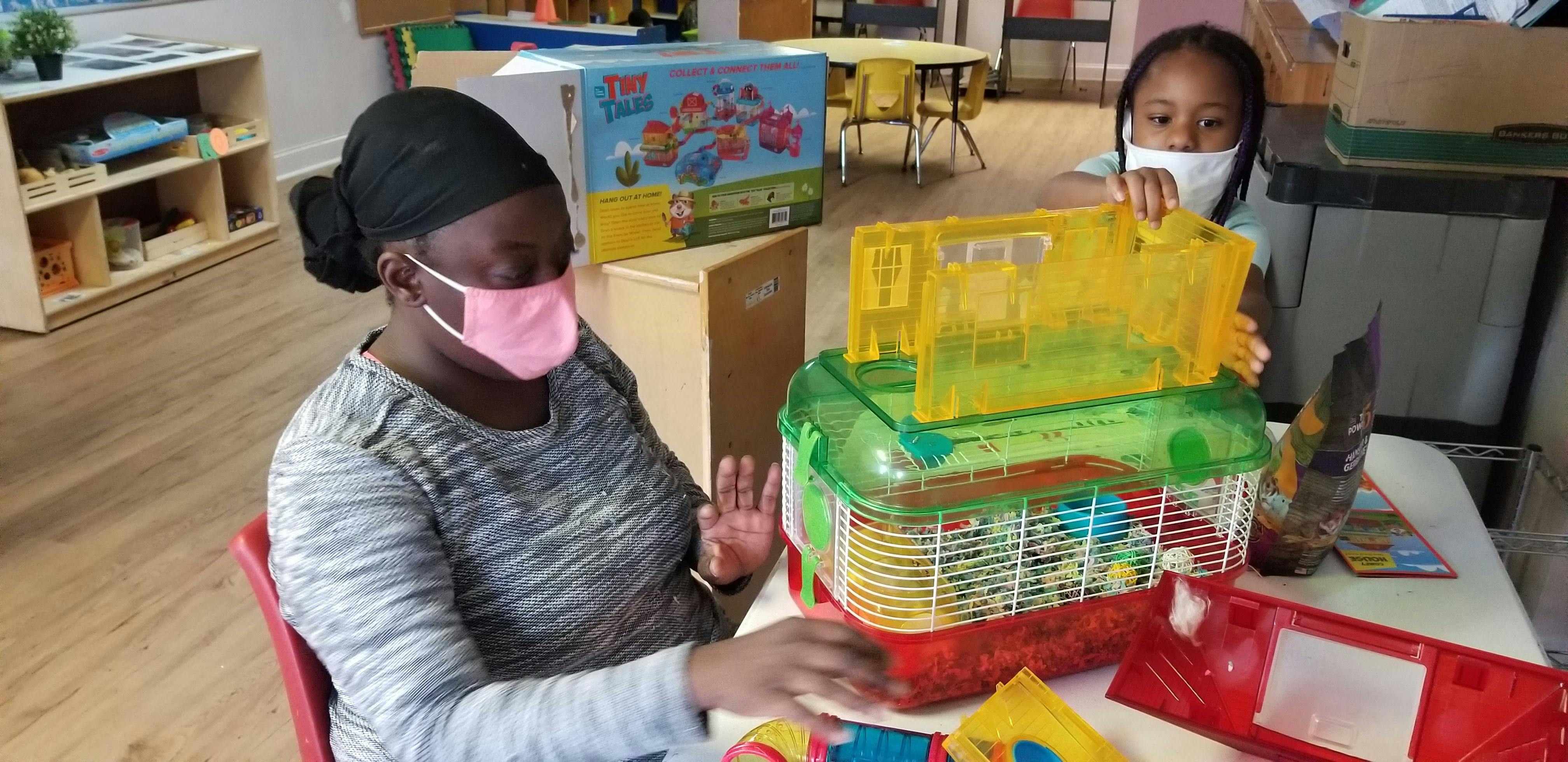 Person and child with face masks looking at a pet cage