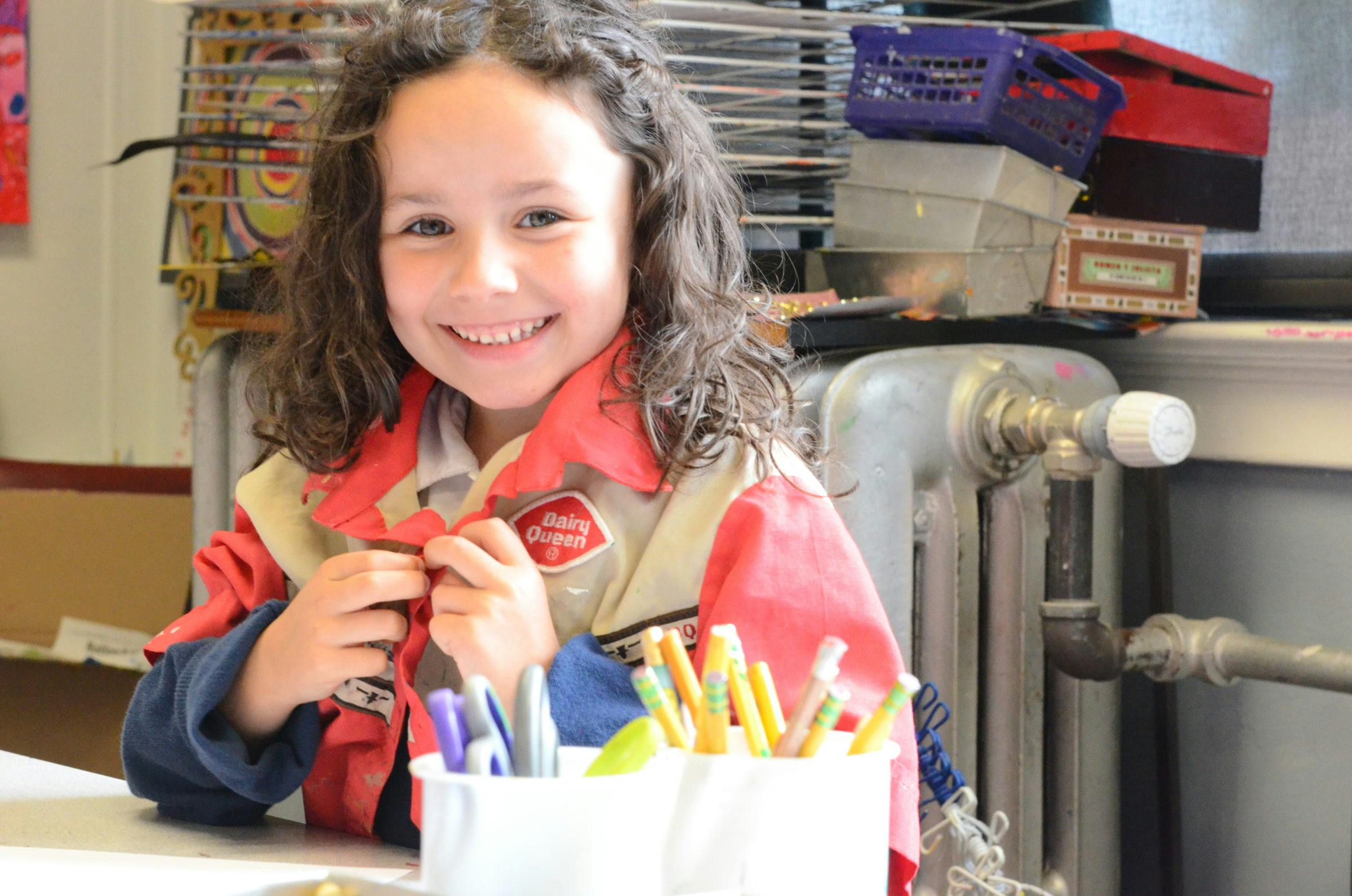 Child in a red and tan jacket sitting at a table with markers