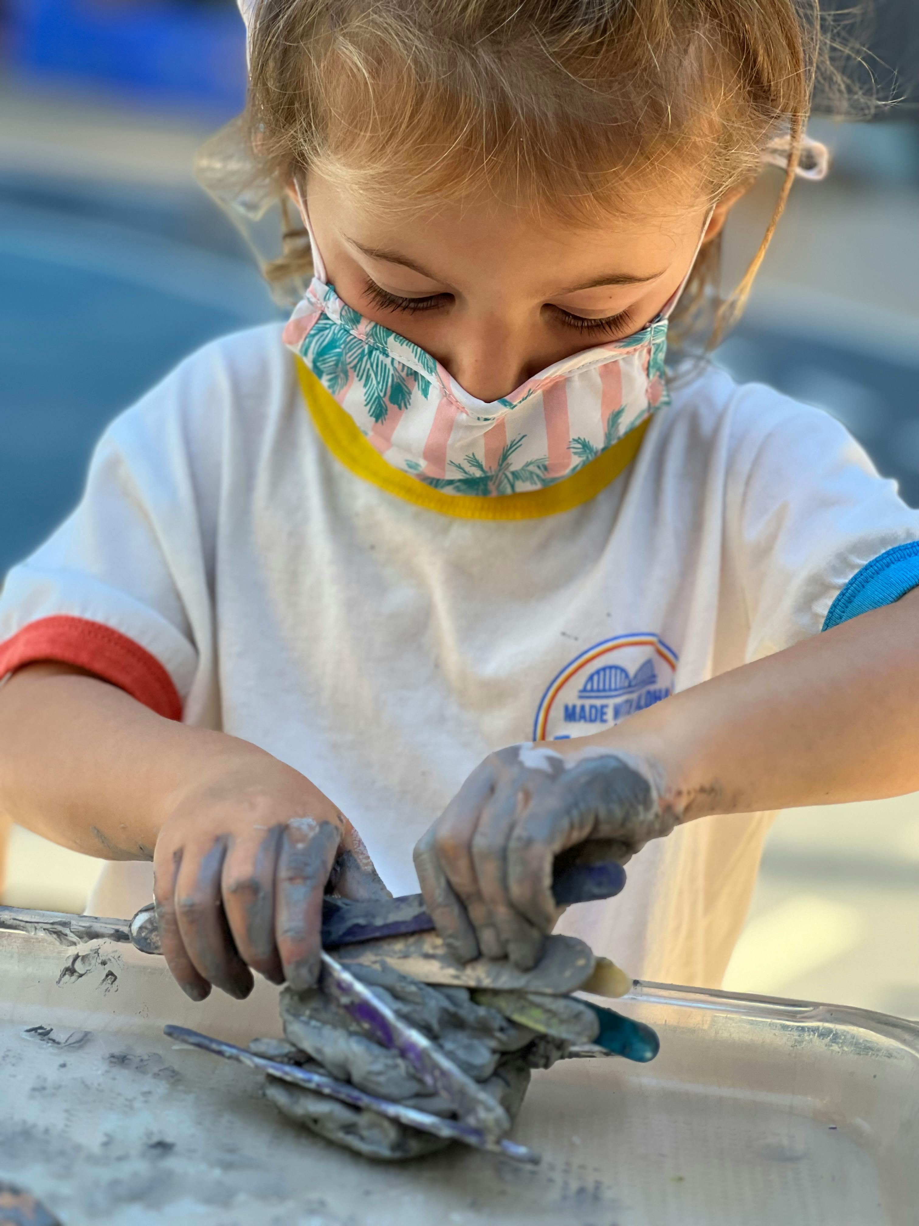 Child in a mask working with clay and tools