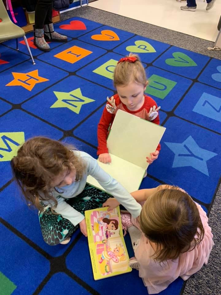 Three children sitting on a rug and looking at books