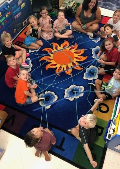 Adult and children sitting on a sun-patterned rug, holding strings