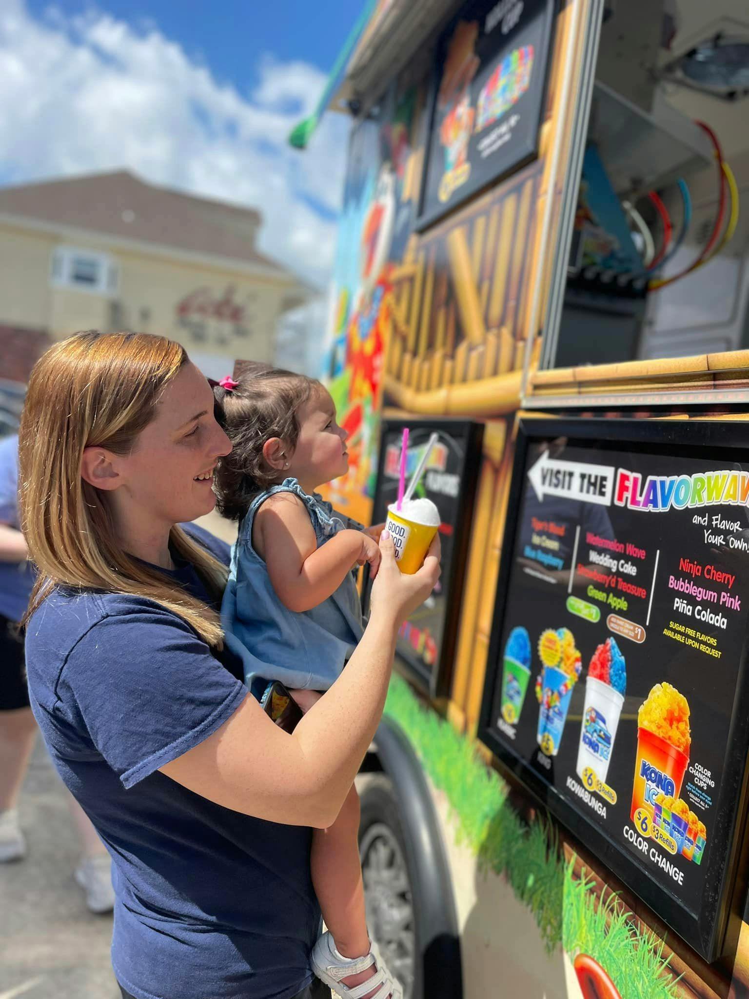 Person holding a child looking at a food truck menu