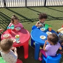 Four children eating snacks at small outdoor tables
