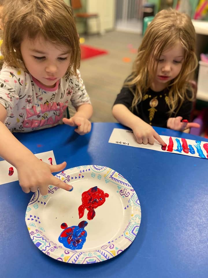 Two children finger painting with red and blue paint