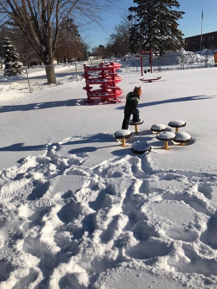 Child standing on a playground stepping stone in the snow