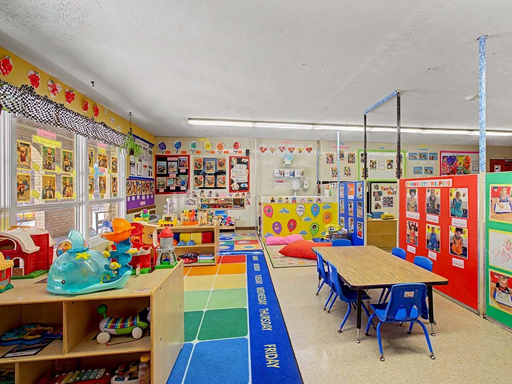 Colorful classroom with play areas, a table and chairs, and bright decorations