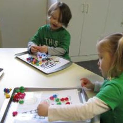 Two children playing with colorful manipulatives on trays