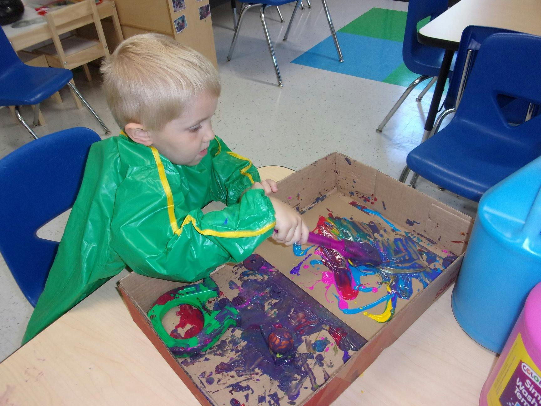 Child in green smock painting in a cardboard box