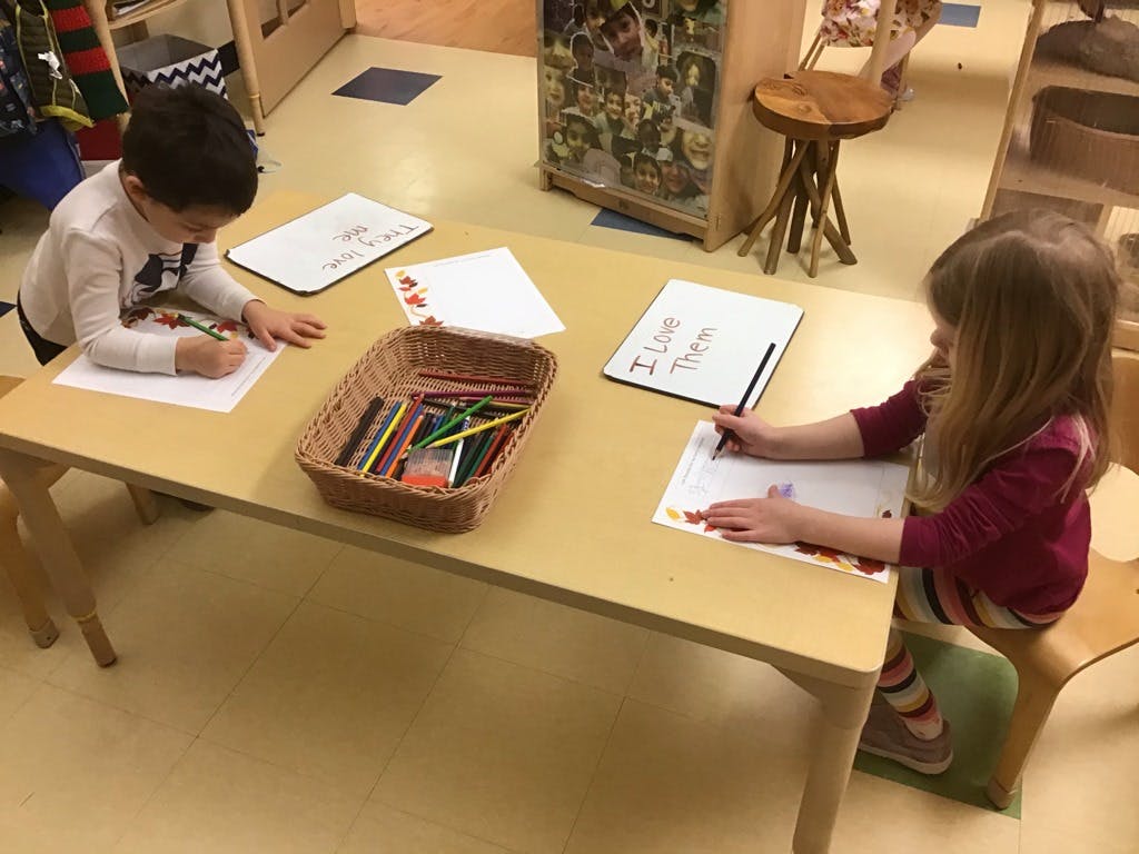 Two children drawing at a table in a classroom