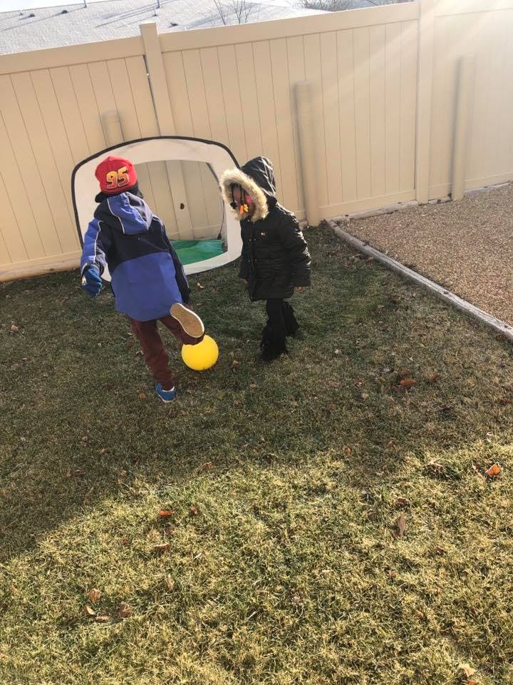 Two children playing with a yellow ball in a grassy yard