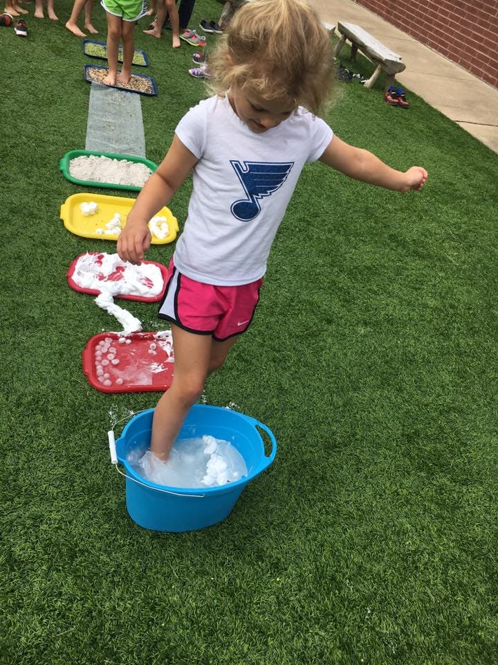 Child stepping into a blue bucket with a foot in water