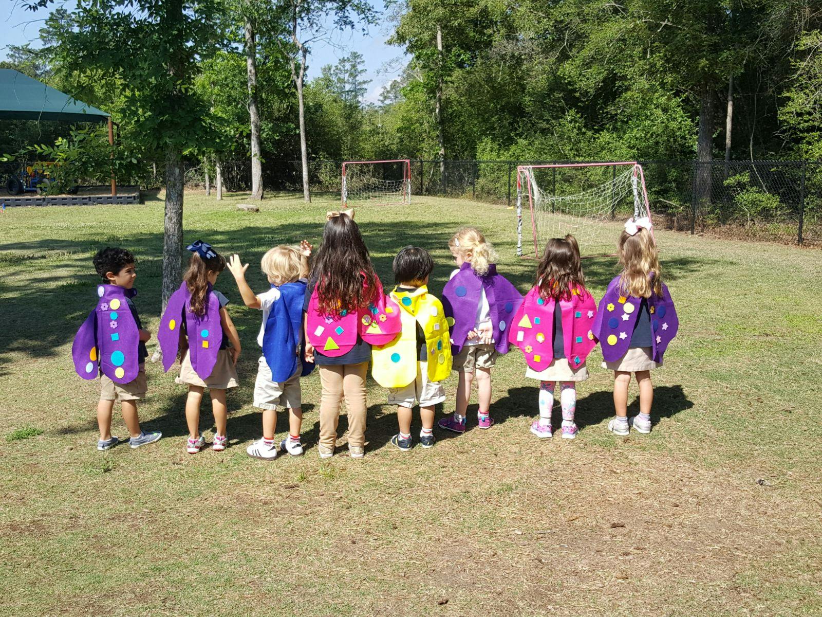 Children in colorful capes standing on a grassy field