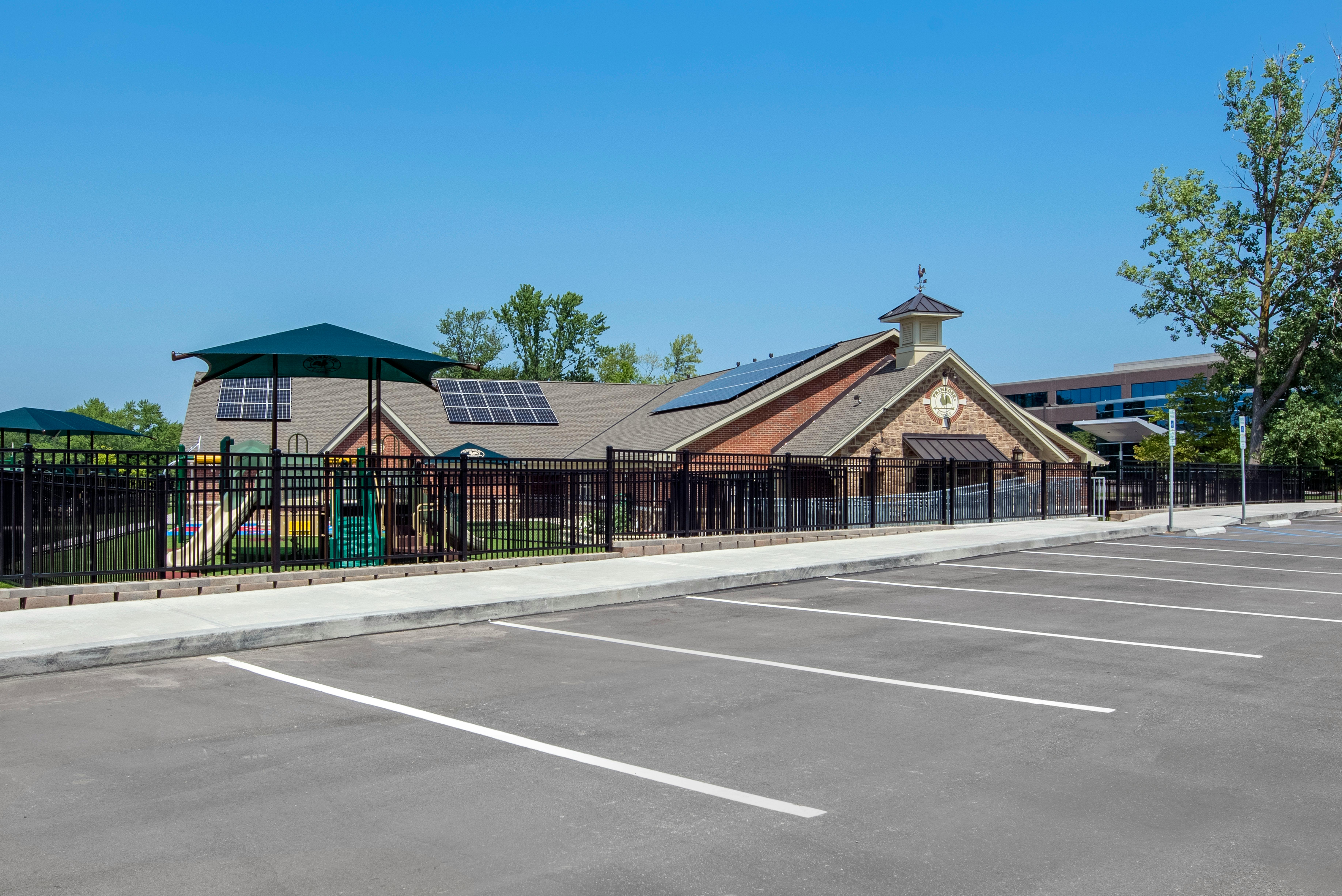 A school building with solar panels on the roof, a playground, and an empty parking lot