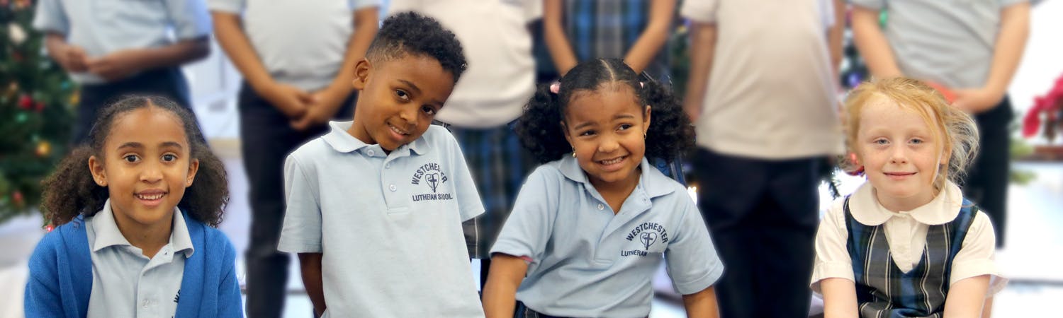 Four children in school uniforms, two boys and two girls, posing for a photo