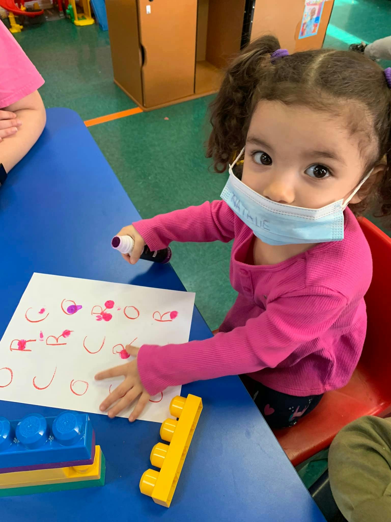 Child in a mask drawing on paper at a table