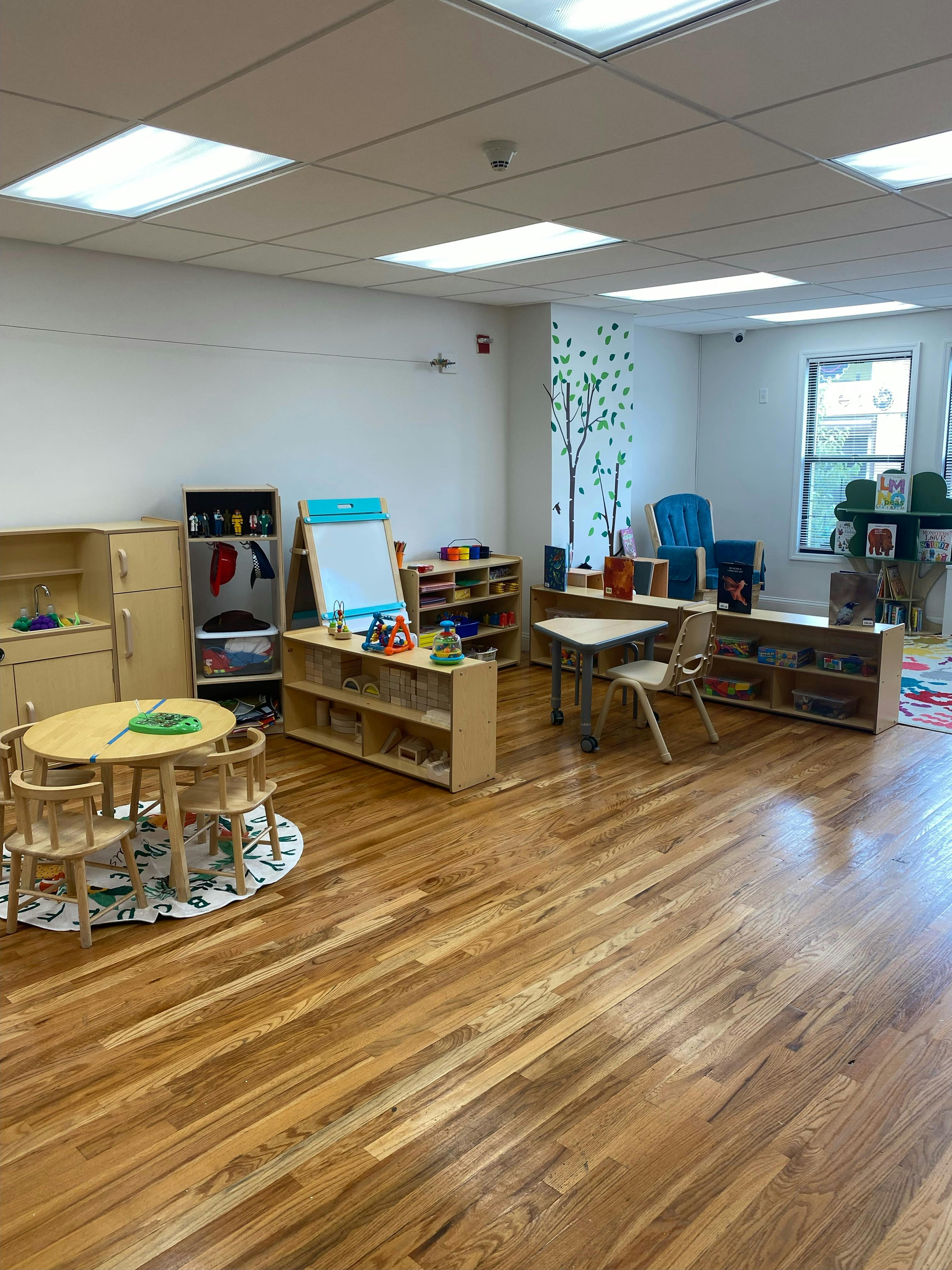 Classroom with small tables and chairs, shelves with toys and books