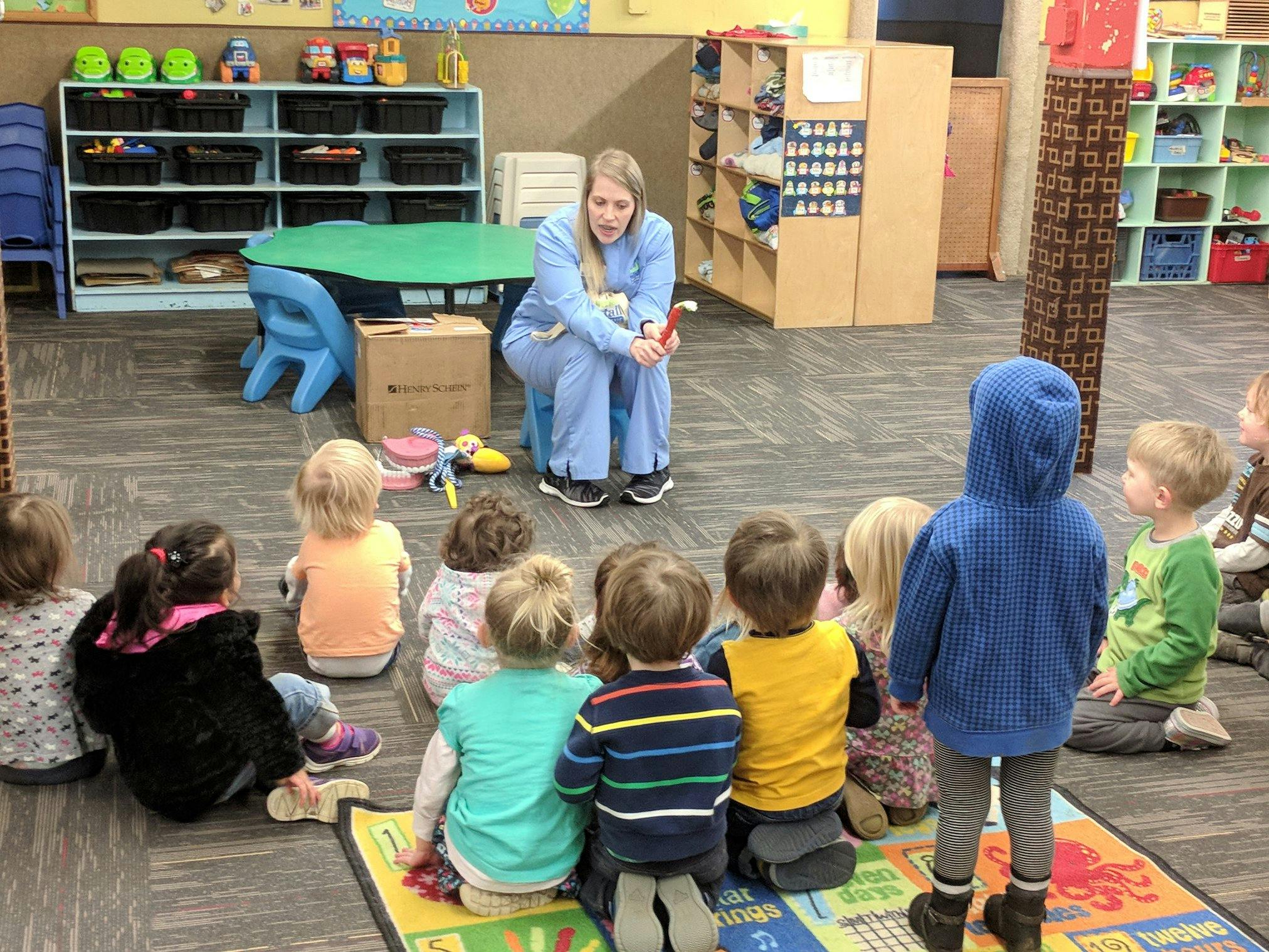 Adult sitting on a low chair reading to a group of children in a classroom
