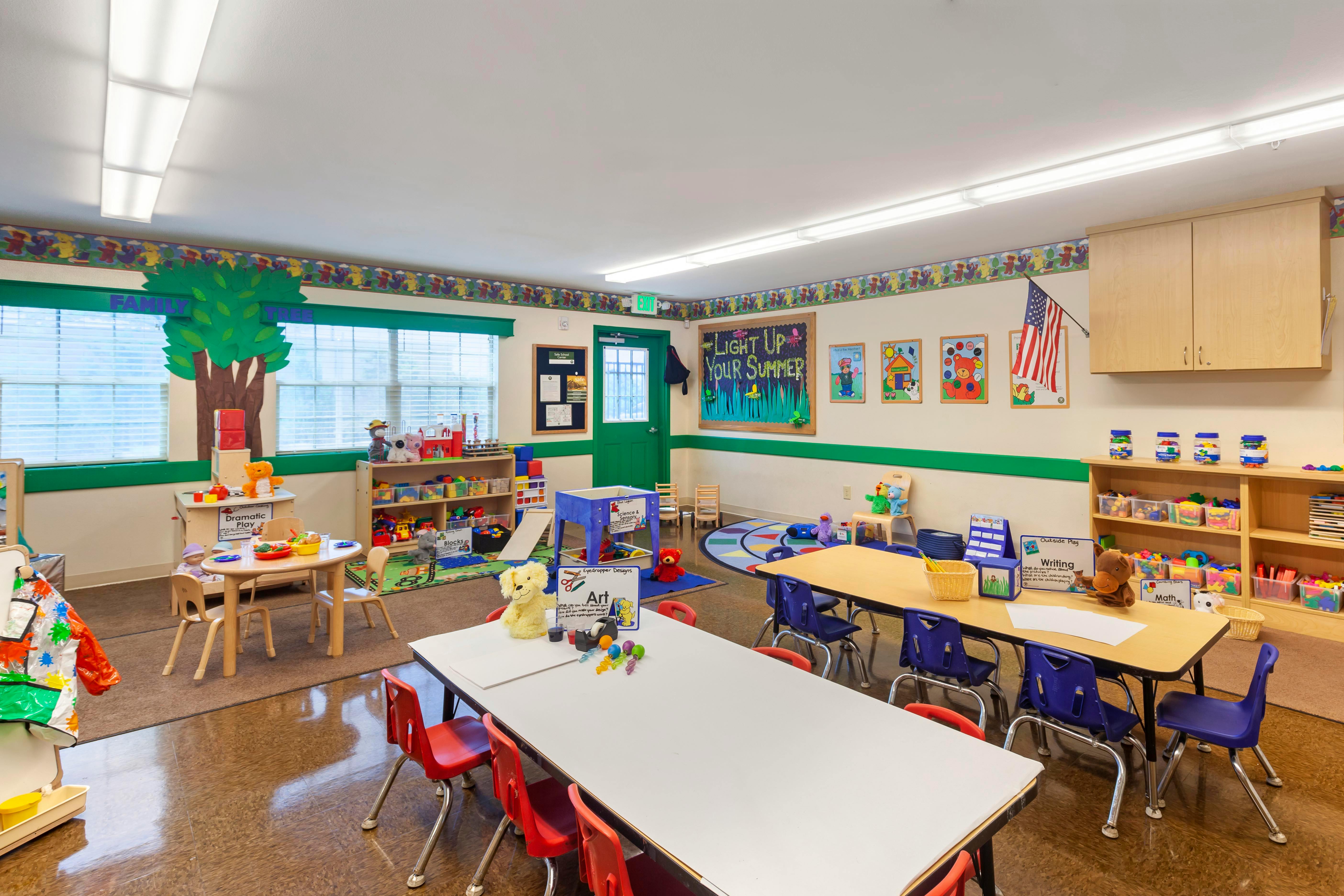 An empty colorful classroom with small tables, chairs, and toys